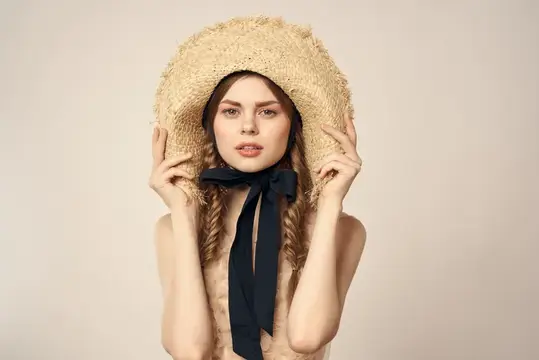 Молодая женщина в соломенной шляпе с чёрной лентой на светлом фоне