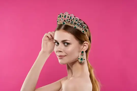 Молодая женщина в роскошной короне с изумрудами на розовом фоне