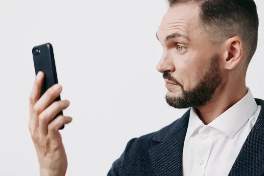Бородатый мужчина в пиджаке удивлённо смотрит на смартфон