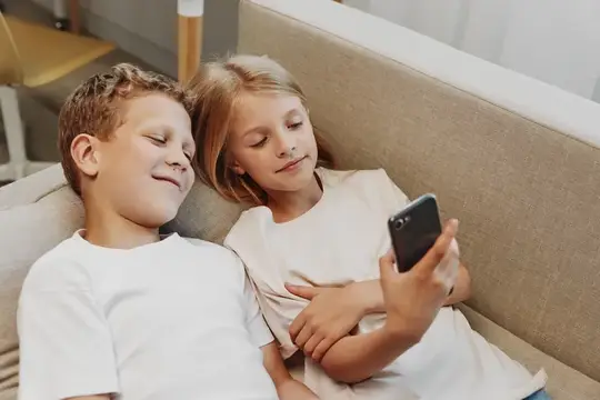 Брат и сестра смотрят в смартфон, лёжа на диване