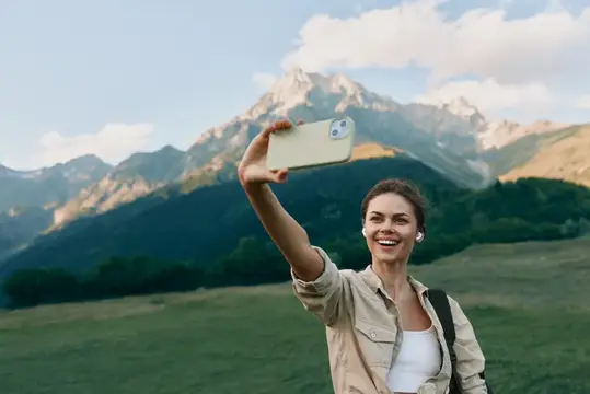 Улыбающаяся девушка делает селфи на фоне гор