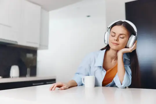 Молодая женщина в наушниках слушает музыку на светлой кухне