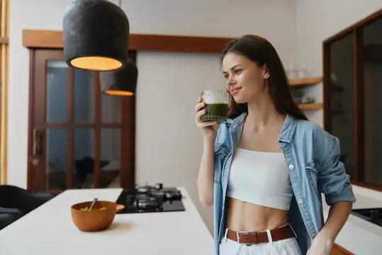 Молодая женщина пьёт зелёный смузи на светлой кухне