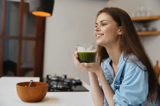Улыбающаяся девушка с стаканом зелёного смузи на кухне