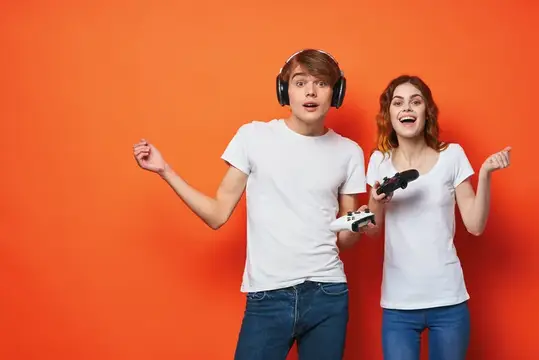 Молодая пара в белых футболках с джойстиками в руках играет в игру на оранжевом фоне