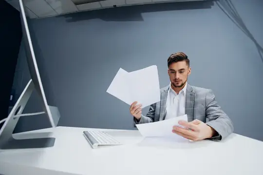 Менеджер работает за компьютером в офисе и разбрасывает документы, выполняя управленческие обязанности