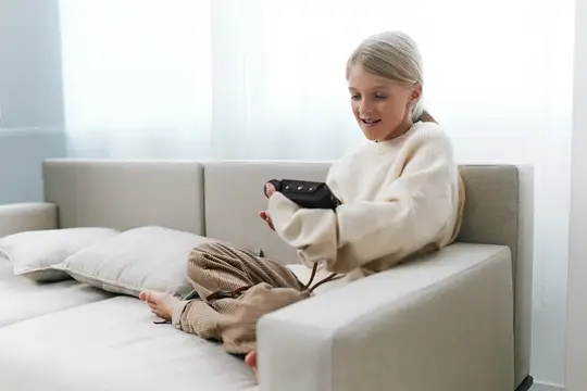 Светловолосая девочка играет в планшет на диване
