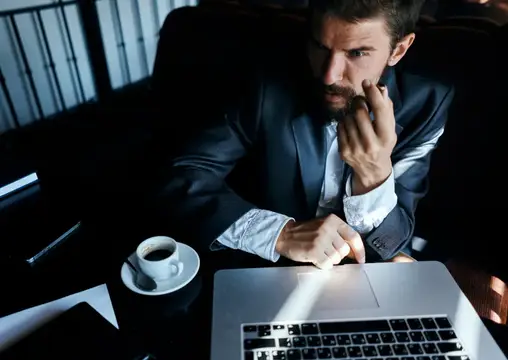 Сосредоточенный мужчина в костюме работает за ноутбуком с чашкой кофе