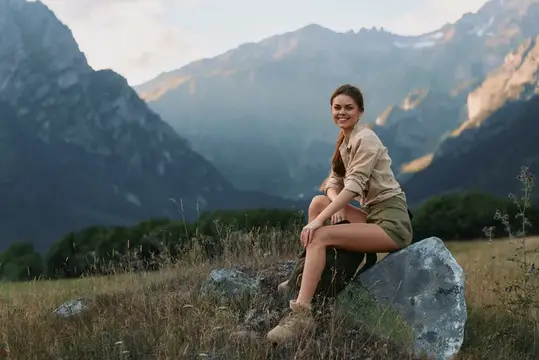 Улыбающаяся девушка сидит на камне на фоне гор
