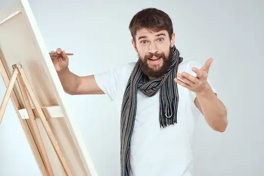 Бородатый мужчина с кистью у мольберта удивлённо жестикулирует