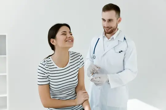 Улыбающийся врач с шприцем готовится сделать укол пациентке