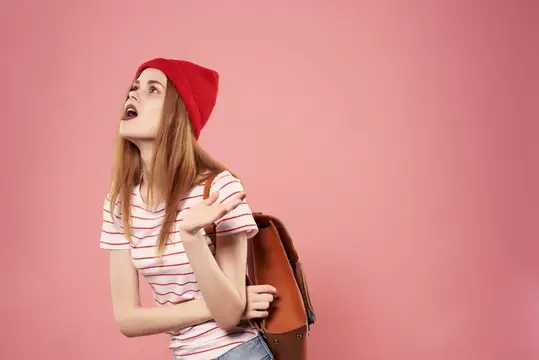 Молодая модная женщина в солнцезащитных очках, одетая в повседневную одежду, позирует на розовом фоне