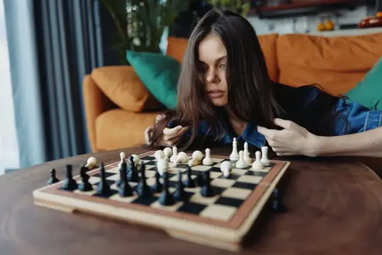 Молодая женщина играет в шахматы на деревянном столе перед диваном на фоне уютной гостиной