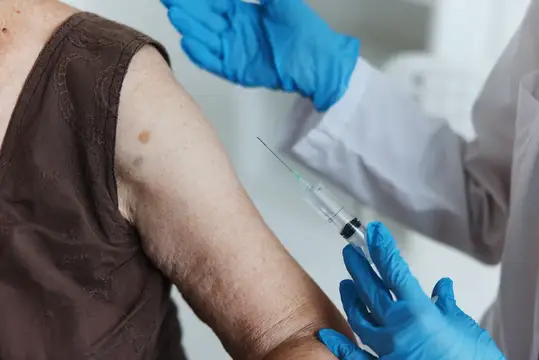 Медик в синих перчатках делает укол в плечо пациенту