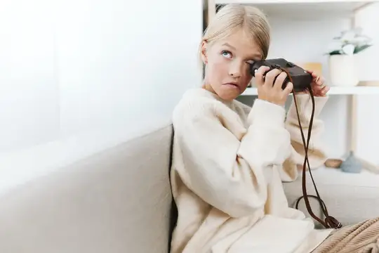 Светловолосая девушка с пленочным фотоаппаратом дома на диване