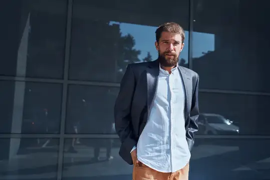Мужчина в деловом костюме стоит на улице возле здания, рядом с ним — официальный бизнесмен