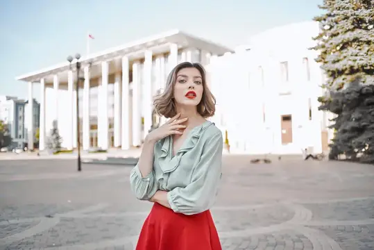 Молодая женщина в блузе и красной юбке на площади у белого здания