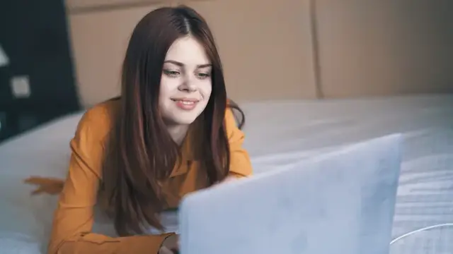 Улыбающаяся девушка лежит на кровати с ноутбуком
