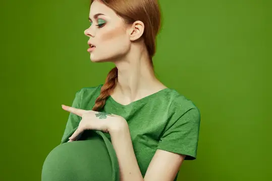 Рыжеволосая девушка с зелёным макияжем и клевером на руке