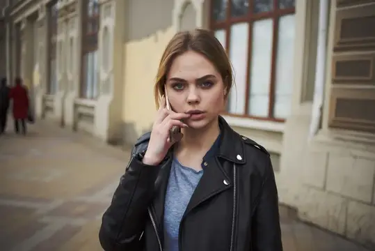 Светловолосая девушка в кожаной куртке говорит по телефону на улице