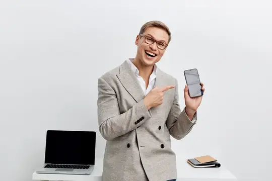 Улыбающийся мужчина в очках и пиджаке показывает на смартфон
