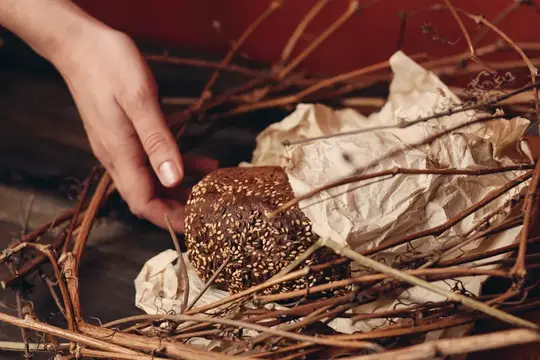 Рука тянется к булочке с кунжутом в плетёной корзине