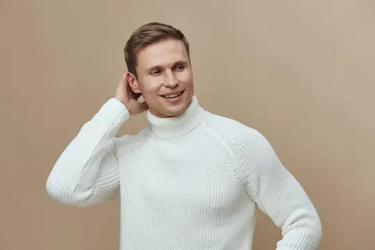 Улыбающийся светловолосый мужчина в белом свитере на бежевом фоне