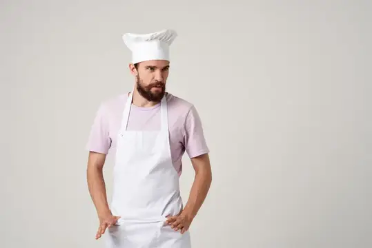 Весёлый шеф-повар мужского пола в белом фартуке жестикулирует руками на кухне ресторана, обращаясь к профессионалам