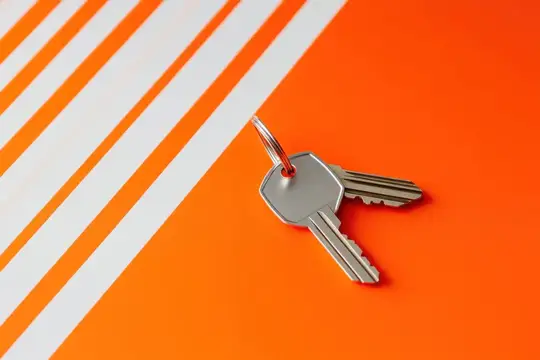 Крупный план стильных металлических ключей на ярком оранжевом фоне с белыми полосами, воплощающий концепции безопасности, доступа и возможностей