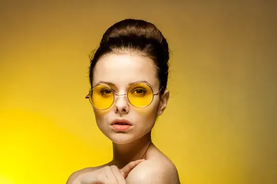 Молодая женщина в круглых желтых очках на желтом фоне