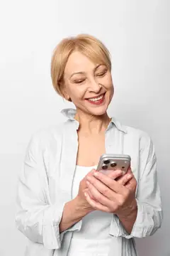 Улыбающаяся блондинка зрелого возраста смотрит в смартфон