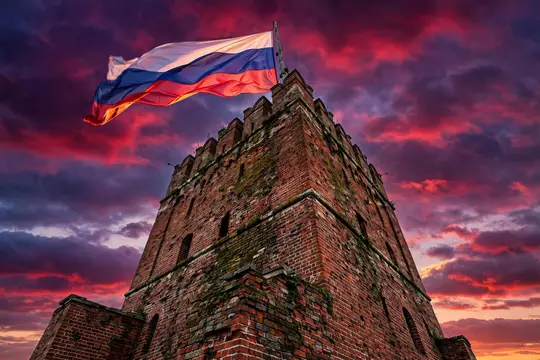 Российский флаг развевается над старинной кирпичной башней на закате