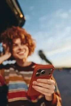 Рыжеволосая девушка со смартфоном улыбается на закате