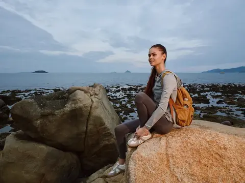 Девушка с рюкзаком отдыхает на камнях у моря