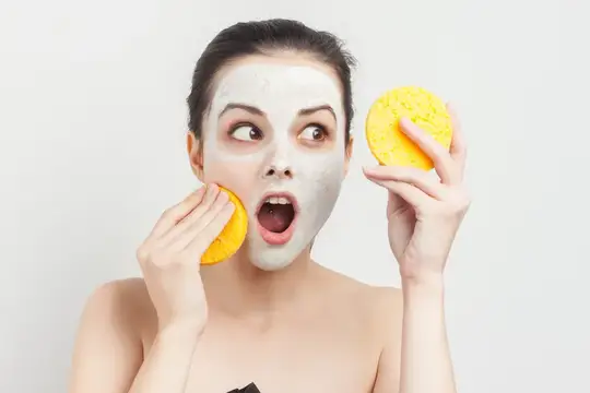 Удивлённая девушка с глиняной маской на лице и жёлтыми спонжами