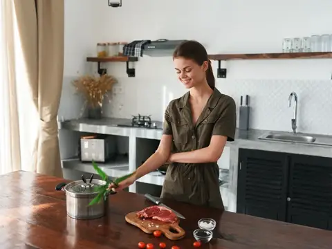 Улыбающаяся девушка готовит мясо на кухне