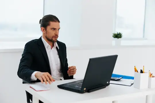 Сосредоточенный мужчина с длинными волосами работает за ноутбуком в офисе