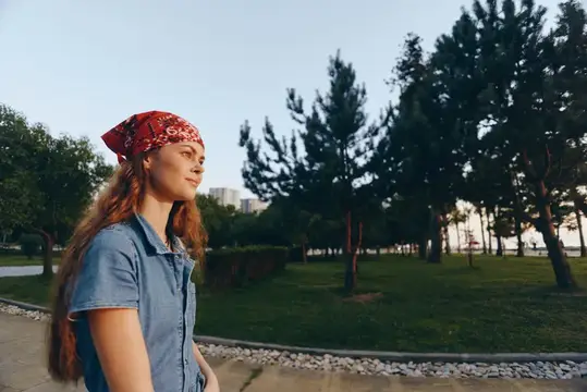 Молодая женщина в красной бандане гуляет по парку летом
