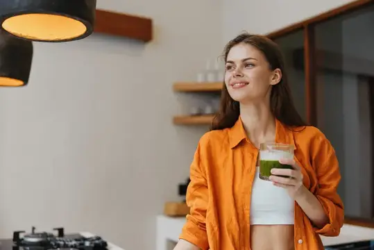 Улыбающаяся девушка с зелёным смузи на светлой кухне