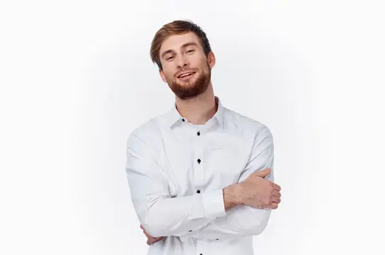 Молодой человек в белой рубашке обнимает себя руками на светлом фоне, вид спереди