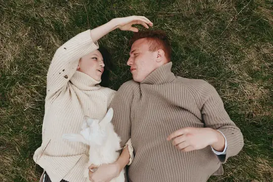 Молодая женщина и мужчина лежат рядом на зеленой траве, одетые в уютные свитера