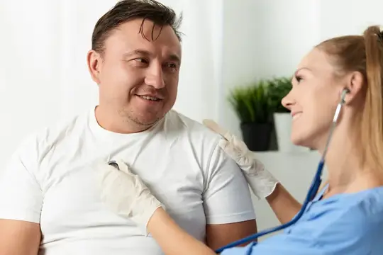 Улыбающийся мужчина на приёме у врача слушает стетоскоп