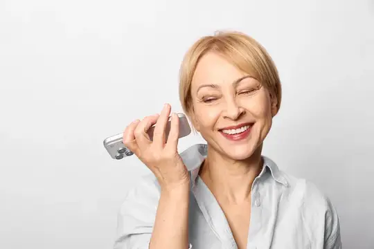 Светловолосая женщина с улыбкой слушает телефон на белом фоне