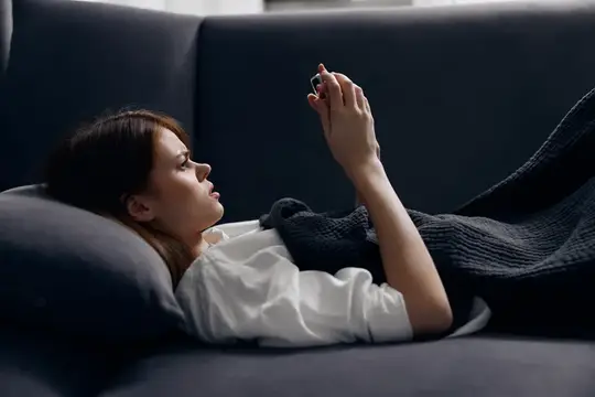 Молодая женщина лежит на диване и смотрит в смартфон