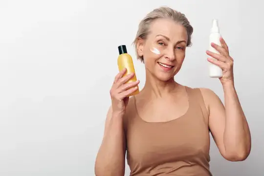 Улыбающаяся седовласая женщина с косметикой в руках на светлом фоне