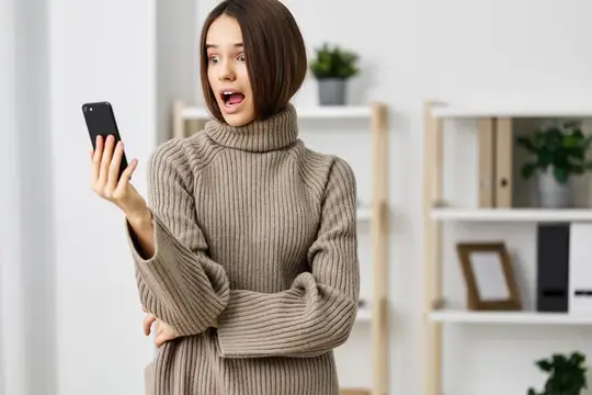 Удивлённая девушка с телефоном в светлой комнате