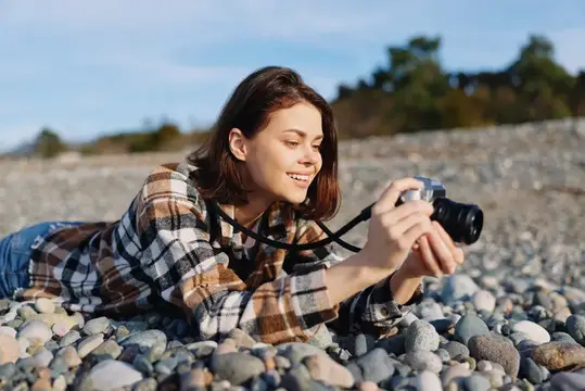 Молодая женщина лежит на каменистом пляже и фотографирует