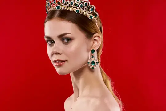 Привлекательная женщина с обнаженными плечами и короной на голове на красном фоне