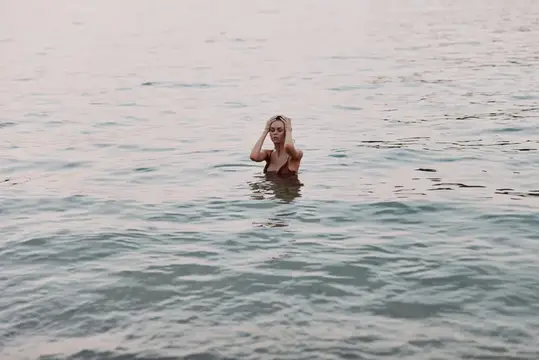 Блондинка по грудь в воде поправляет волосы в пасмурный день