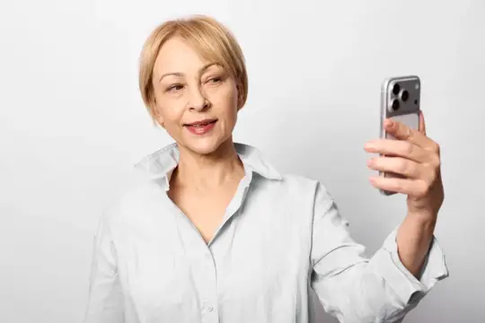 Светловолосая женщина делает селфи на смартфон на светлом фоне